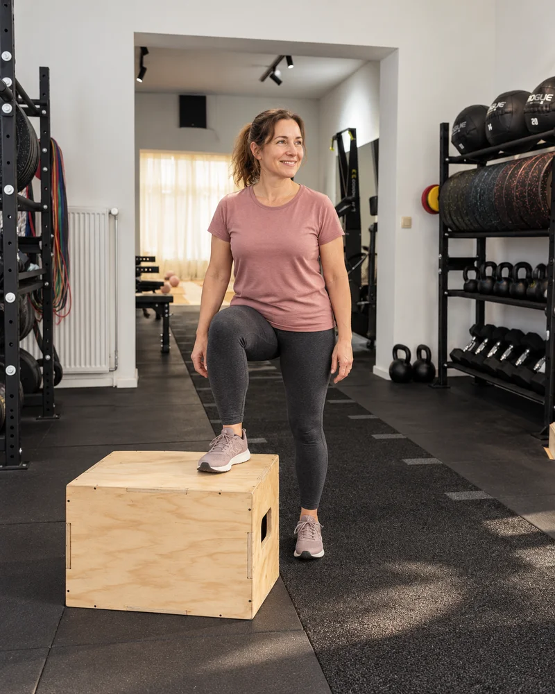 Une femme monte sur une box en bois, un pied posé sur le dessus